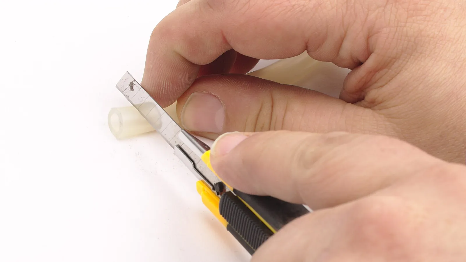 Hands cutting a length of clear hose tubing with a utility knife