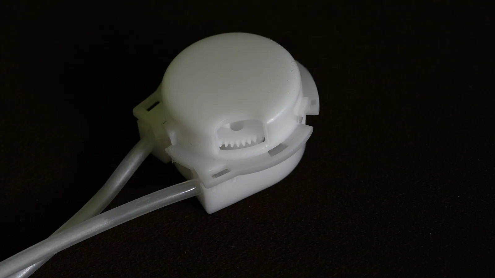 Closed and latched white peristaltic pump head with two translucent tubes seated in its side ports, ready for a test run