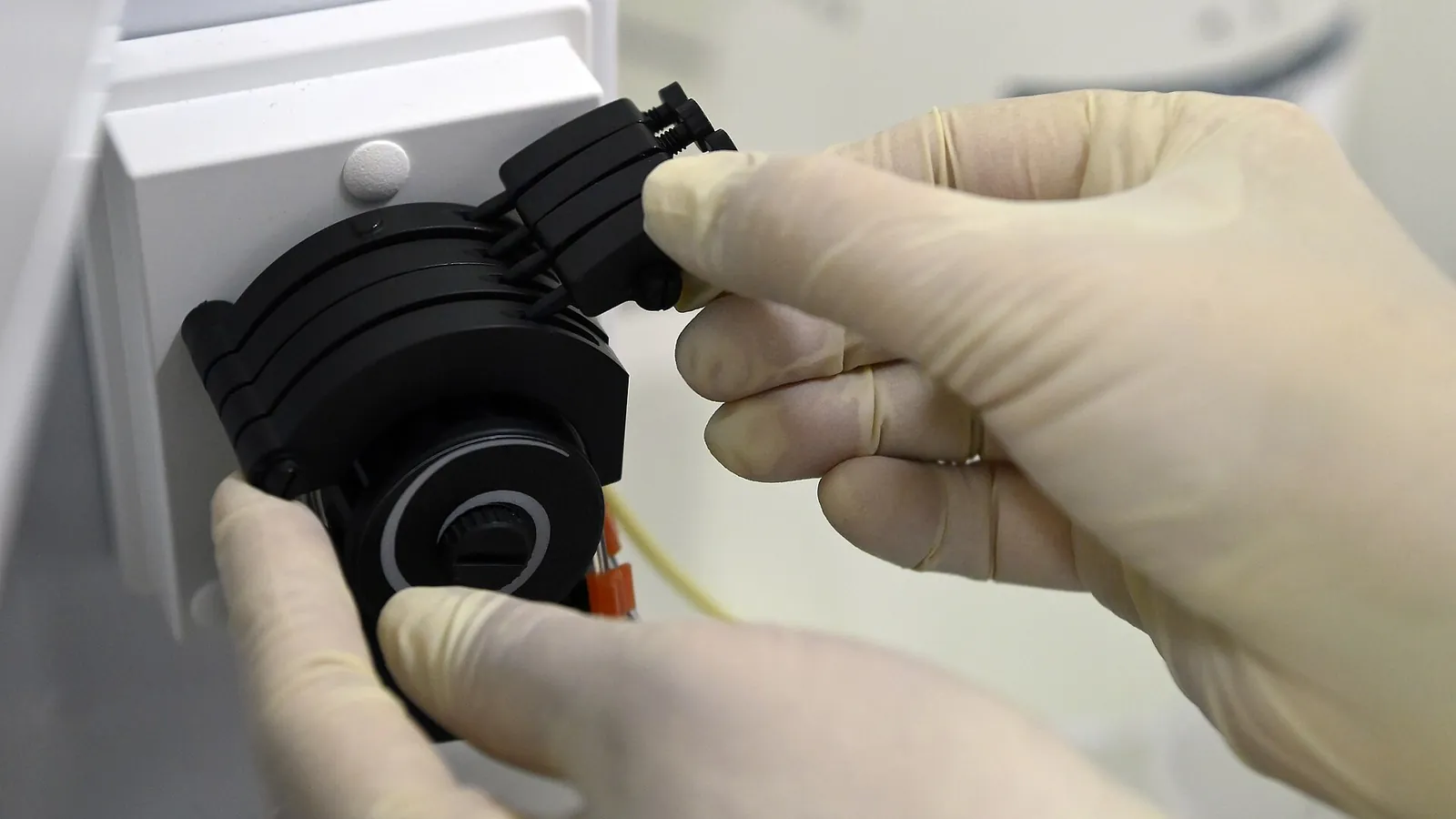 Gloved hands installing a peristaltic pump head on laboratory equipment