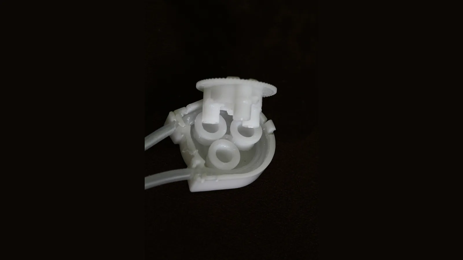 Peristaltic pump head with three rollers and tubing, full view on dark background